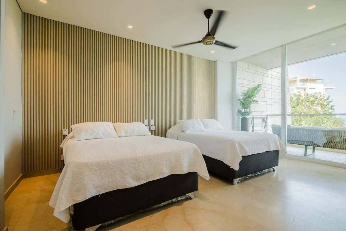 A modern hotel room with two beds, a ceiling fan, and a balcony with a view.