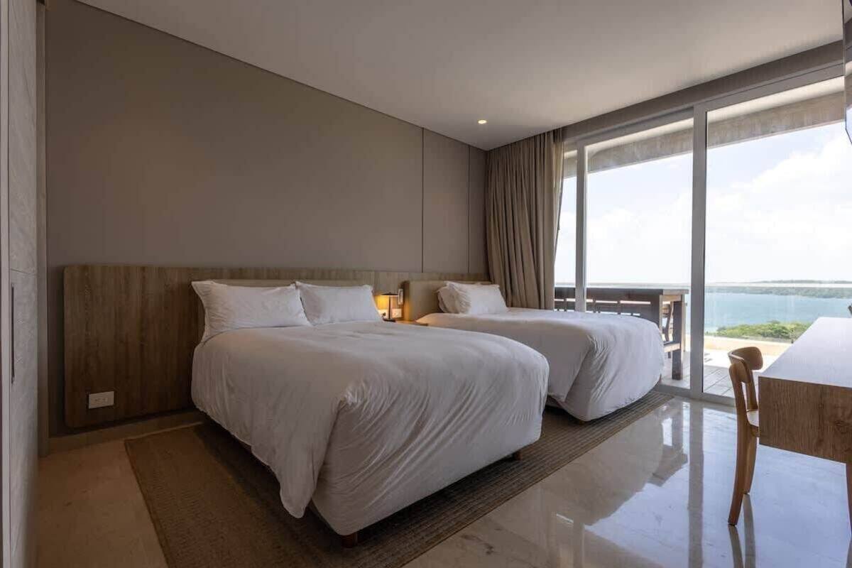 A modern hotel room with two beds, a balcony with a view, and a large window.