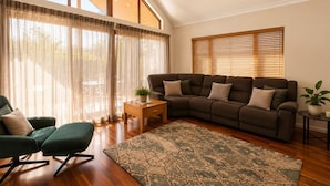 A living room with a sectional sofa, a green armchair, a small table with a plant, and a patterned rug. - Bay Breeze on Thomas (West Busselton)