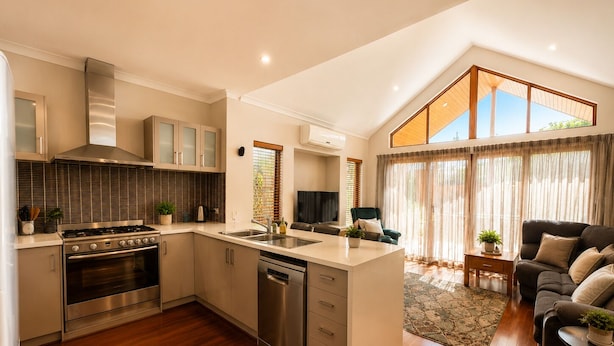 A modern kitchen with a central island, stainless steel appliances, and a dining area with a sofa and a small table. - Bay Breeze on Thomas (West Busselton)