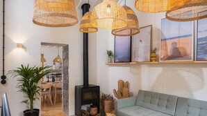 A cozy living room with a sofa, a fireplace, wicker pendant lights, and a dining area with a table and chairs. - ALMA - Island House by GuestReady (Faial da Terra)
