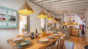 A dining area with a wooden table set for four, hanging woven pendant lights, and a kitchen in the background. - ALMA - Island House by GuestReady (Faial da Terra)