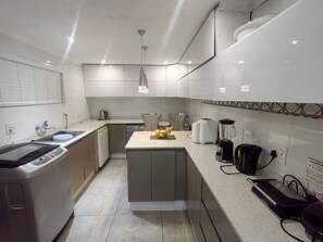 Een moderne keuken met witte kastjes, een centraal eiland, een koffiezetapparaat, een blender en een waterkoker.