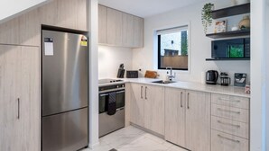 Cozinha moderna com eletrodomésticos de aço inoxidável, armários de madeira clara e uma janela que permite entrada de luz natural.
