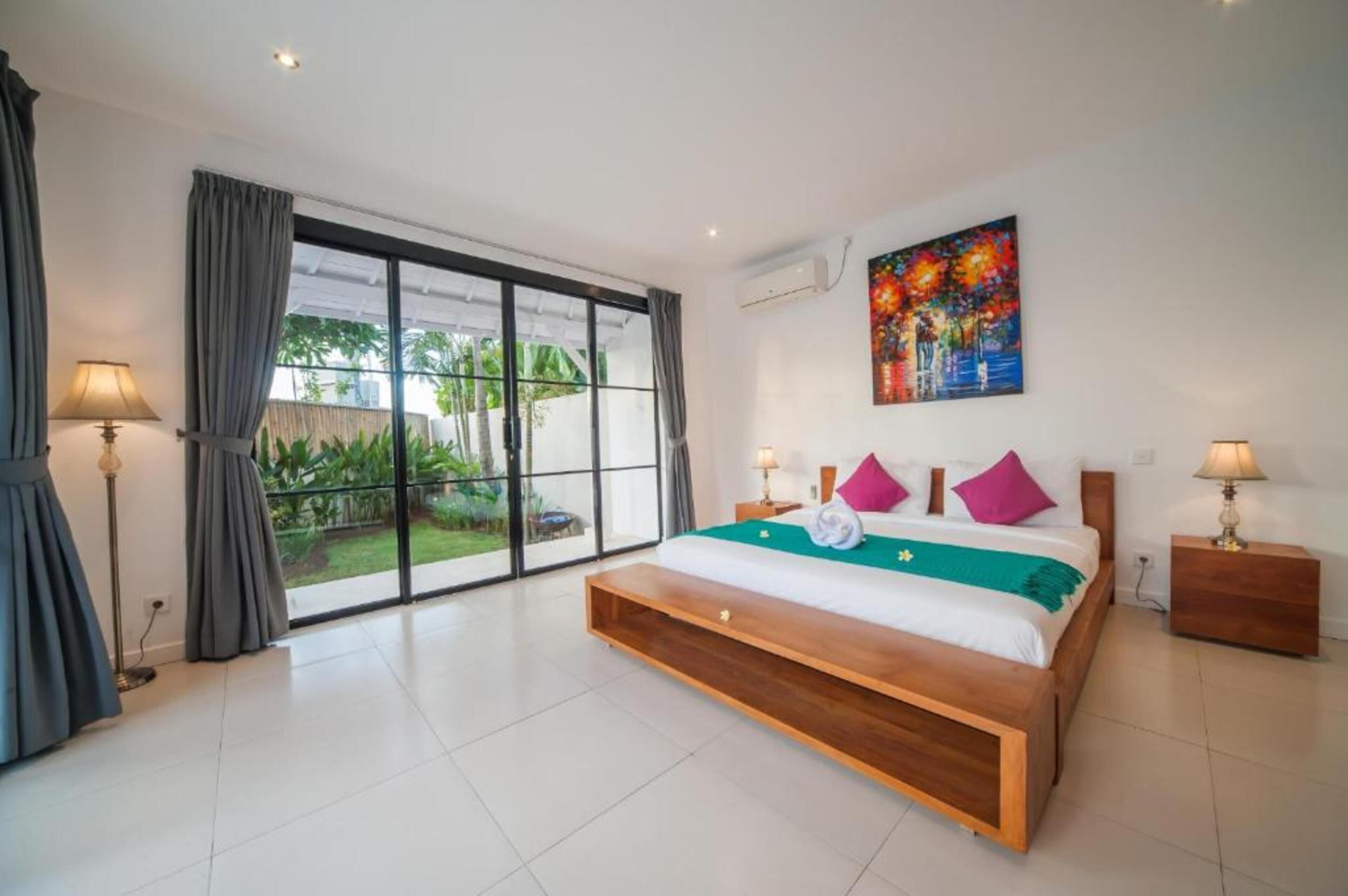 A modern bedroom with a large bed, a painting, and a view of a garden through a sliding door.