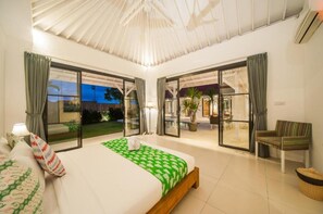 A bedroom with a large bed, sliding glass doors leading to a balcony, and a chair. - Specious 3Bedroom Rakuen Villa Canggu (Canggu)