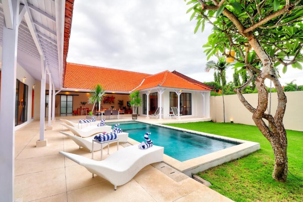 A swimming pool with lounge chairs, a covered patio, and a well-maintained lawn.