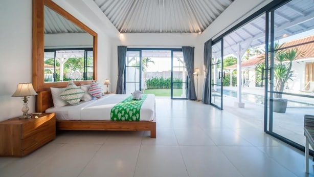 A modern bedroom with a large bed, a nightstand, a mirror, and a view of a pool and outdoor area. - Specious 3Bedroom Rakuen Villa Canggu (Canggu)