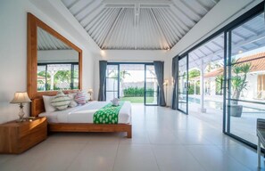A modern bedroom with a large bed, a nightstand, a mirror, and a view of a pool and outdoor area. - Specious 3Bedroom Rakuen Villa Canggu (Canggu)