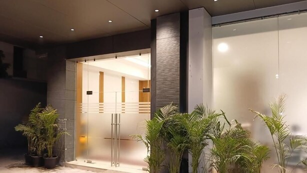 A modern building entrance with a glass door, potted plants, and a visible interior through the glass.