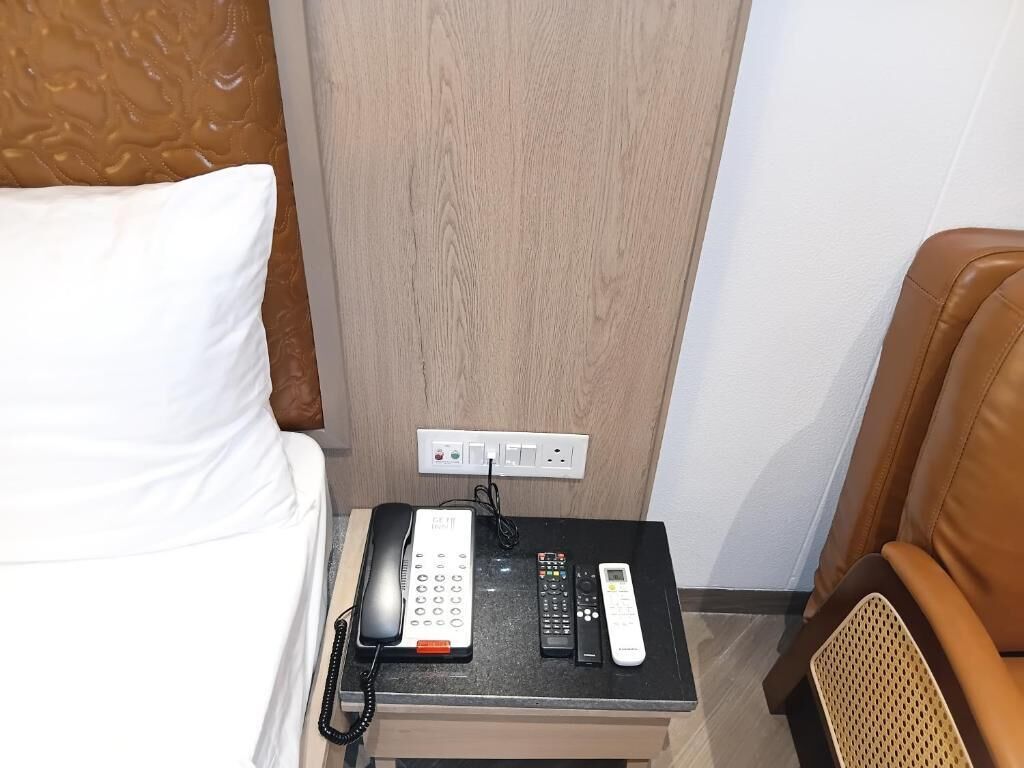 Een hotelkamer met een bed, nachtkastje, telefoon, afstandsbedieningen en een stopcontact.