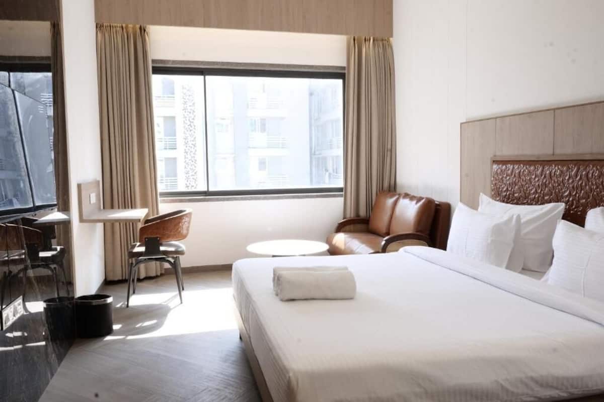 Una habitación de hotel con cama, escritorio, silla, televisor y ventana con cortinas.