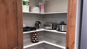 Ett hörnskafferi med hyllor, en kaffebryggare, en brödrost och en pall.