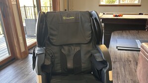 En massagefåtölj med en kontrollpanel, ett biljardbord och ett fönster med utsikt över träd.