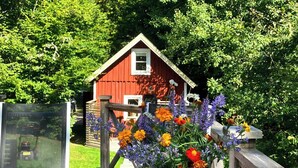 Ett rött trähus med ett vitt fönster och en vit dörr, omgivet av frodiga, gröna träd.