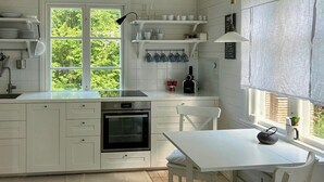 Ett kök med vita skåp, en spis, ett diskho och ett fönster med utsikt över grönområden.