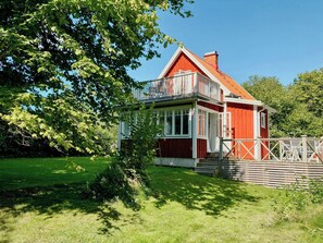 Una casa de madera roja con balcón, rodeada por un patio cubierto de césped y árboles.