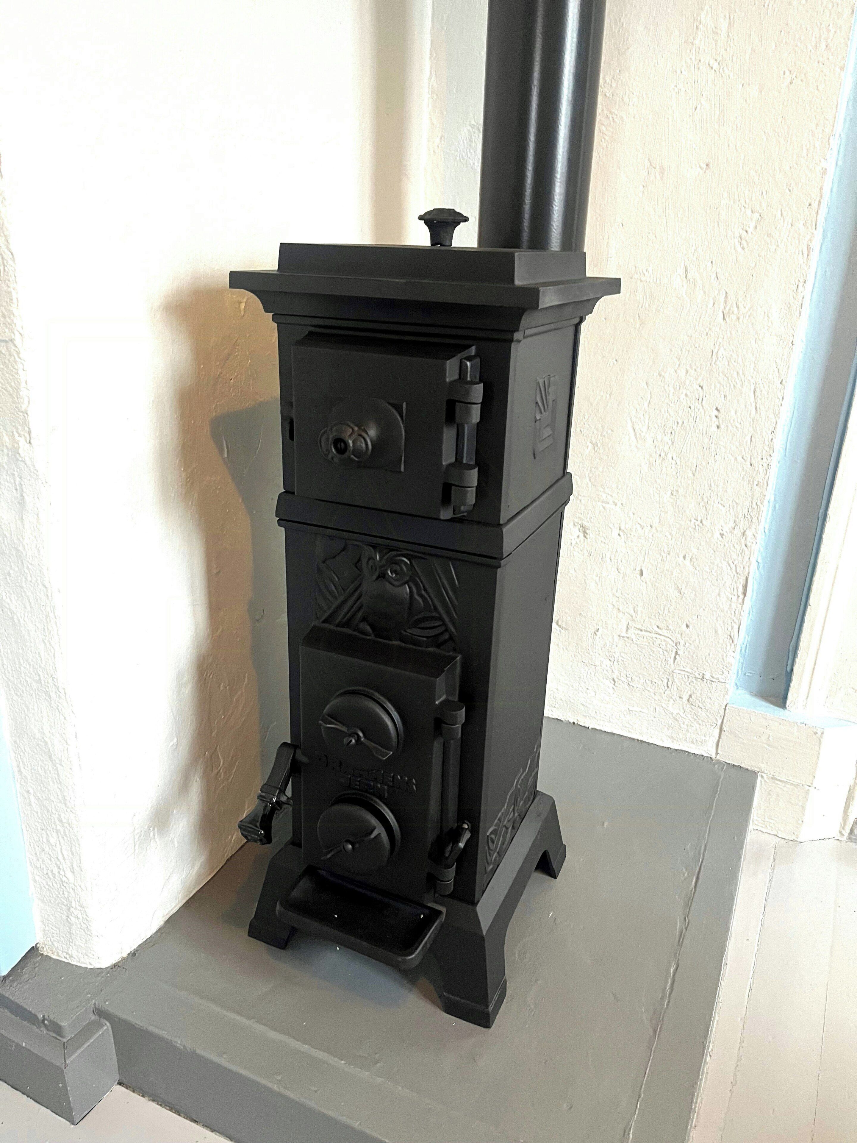 Una estufa de leña negra con chimenea, un panel de control y una pequeña ventana.