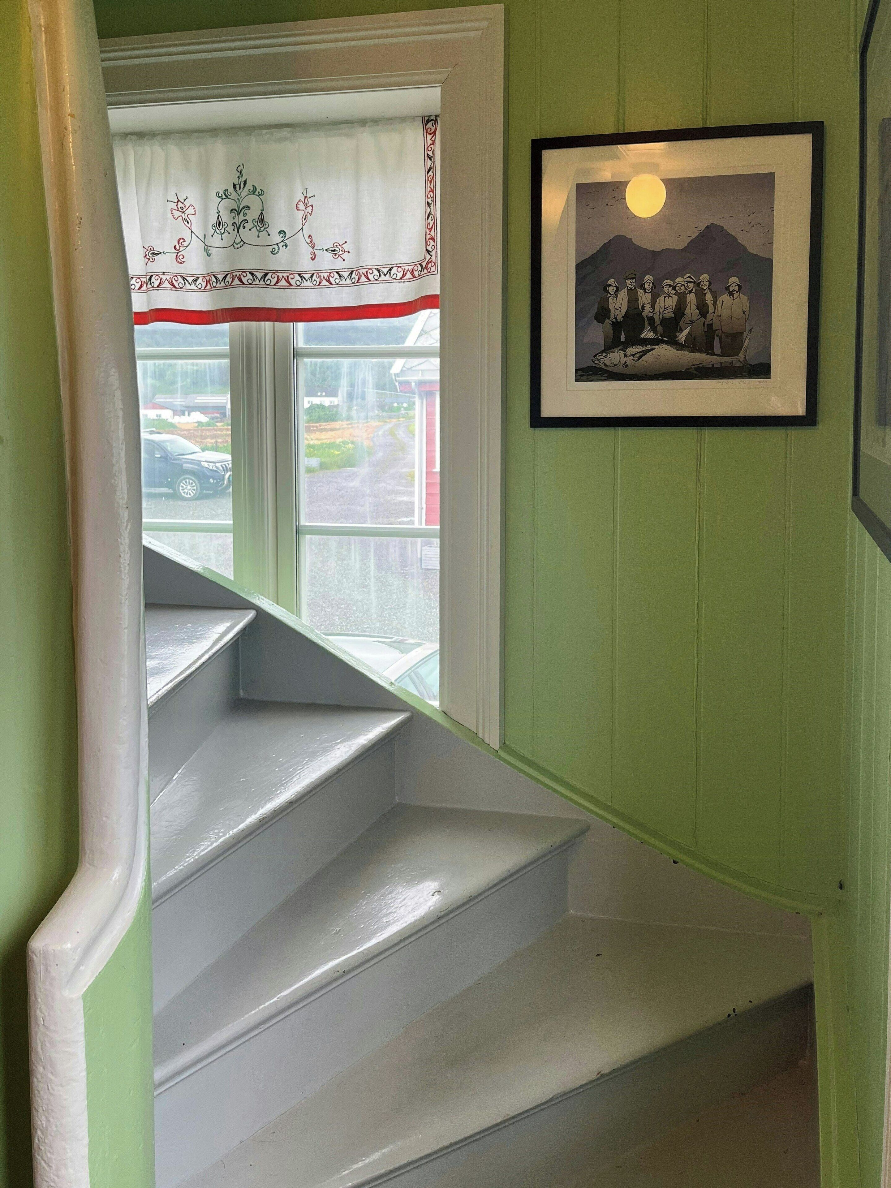 Un escalier aux marches blanches et une fenêtre ornée d’un rideau blanc bordé de rouge.