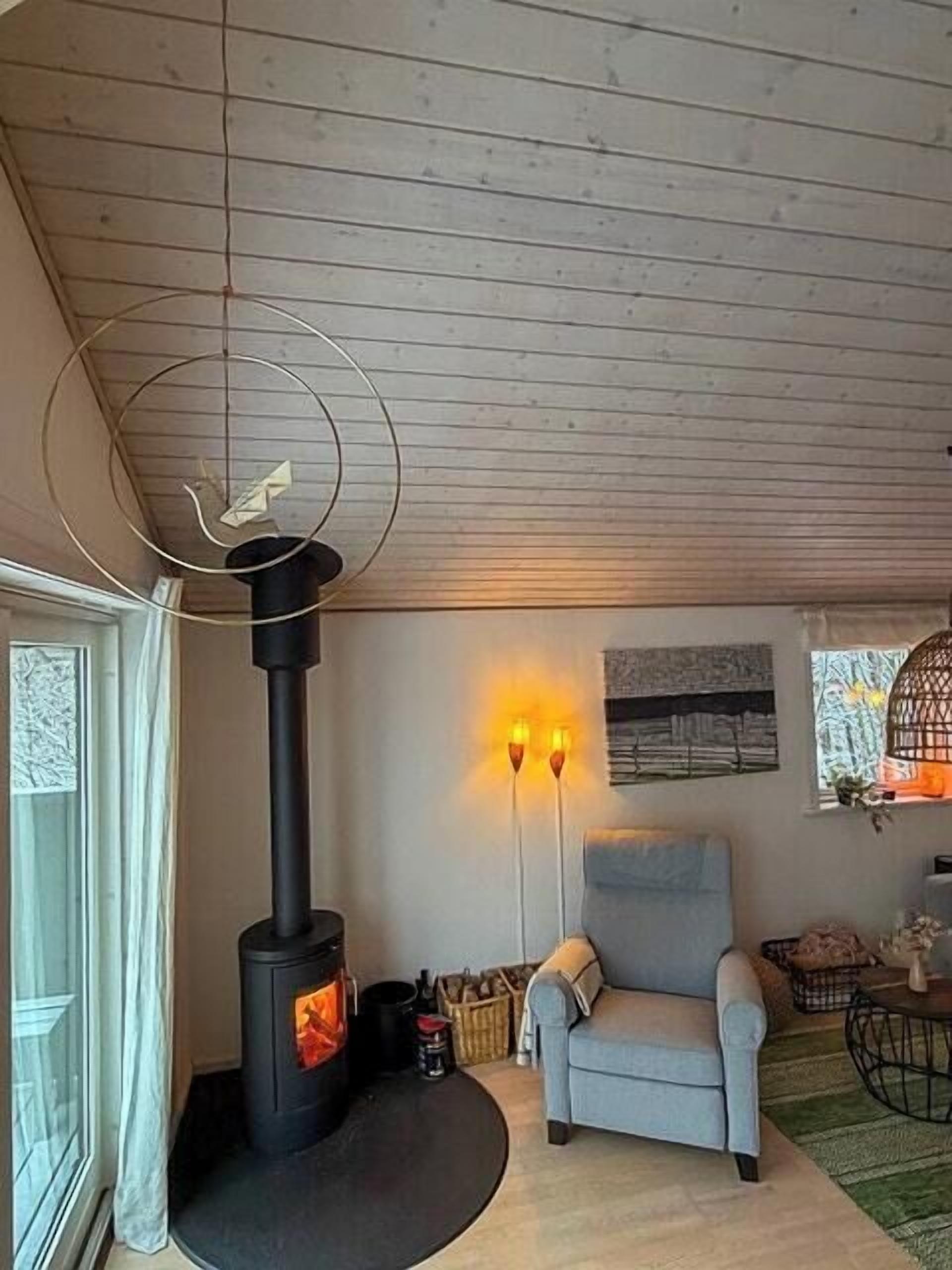 A cozy living room with a wood-burning stove, a comfortable armchair, and a large window with artwork.