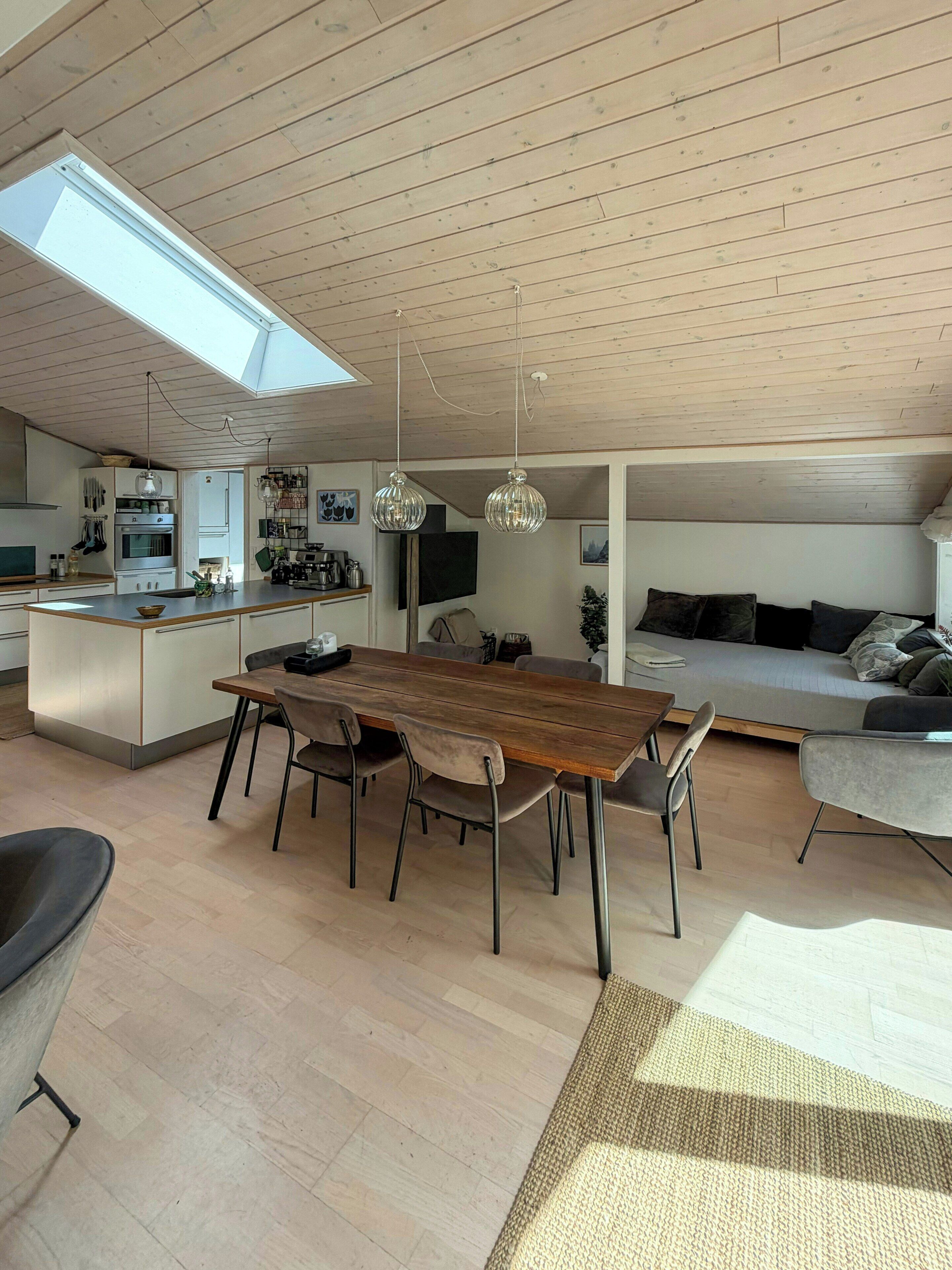 A modern kitchen with a central island, a dining area with a wooden table and chairs, and a cozy living space with a sofa and pillows.