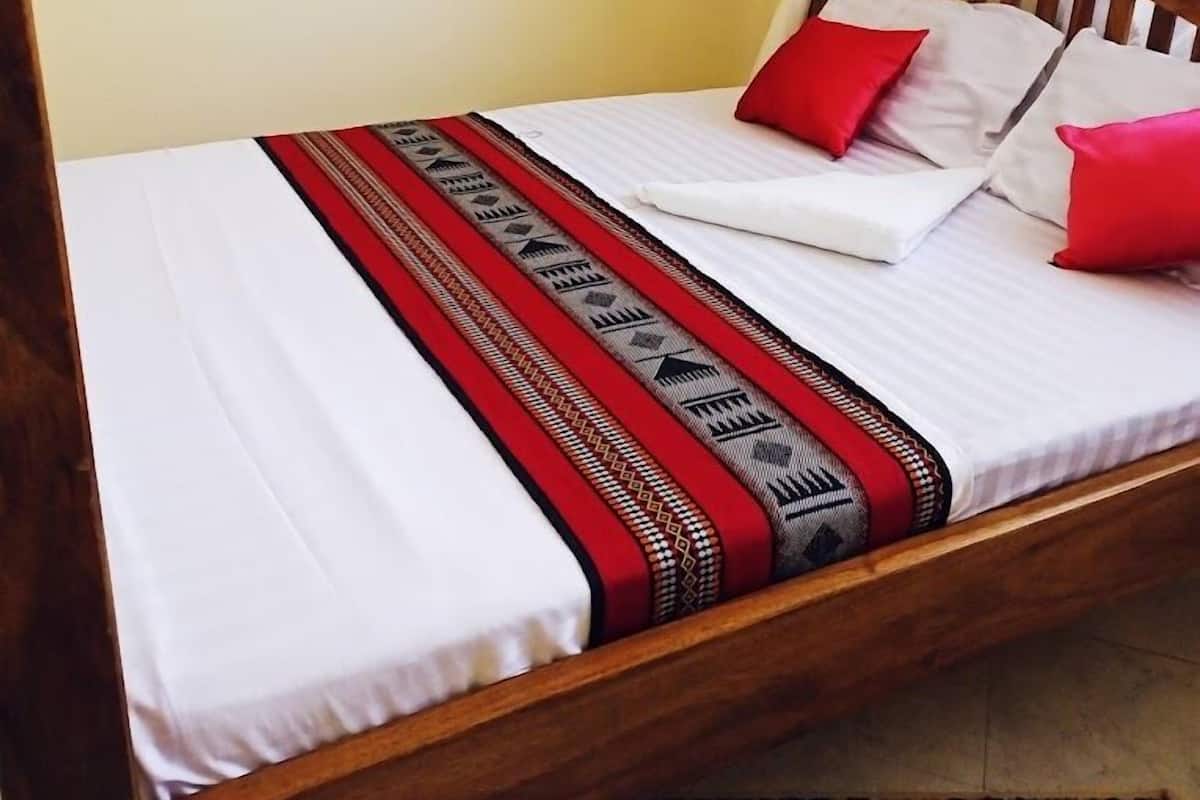 Una cama con dosel, ropa de cama blanca y una manta estampada.