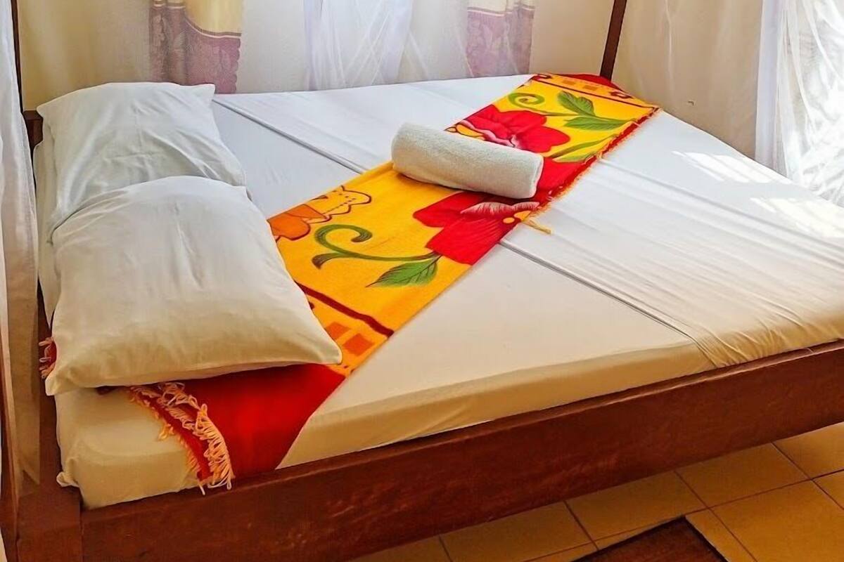 Una cama individual con colcha estampada, almohadas blancas y dosel blanco.