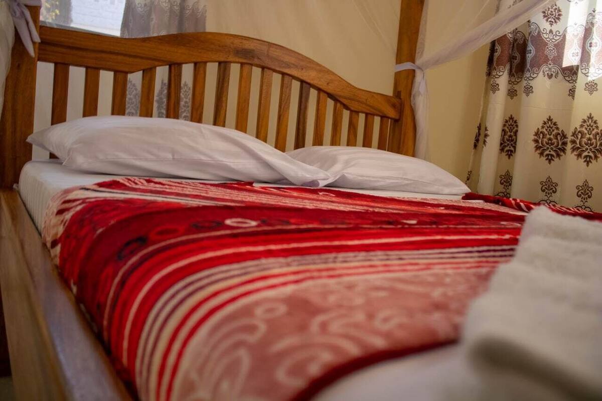 Una cama de madera con colcha de diseño rojo y blanco, almohadas blancas y cabecera de madera.