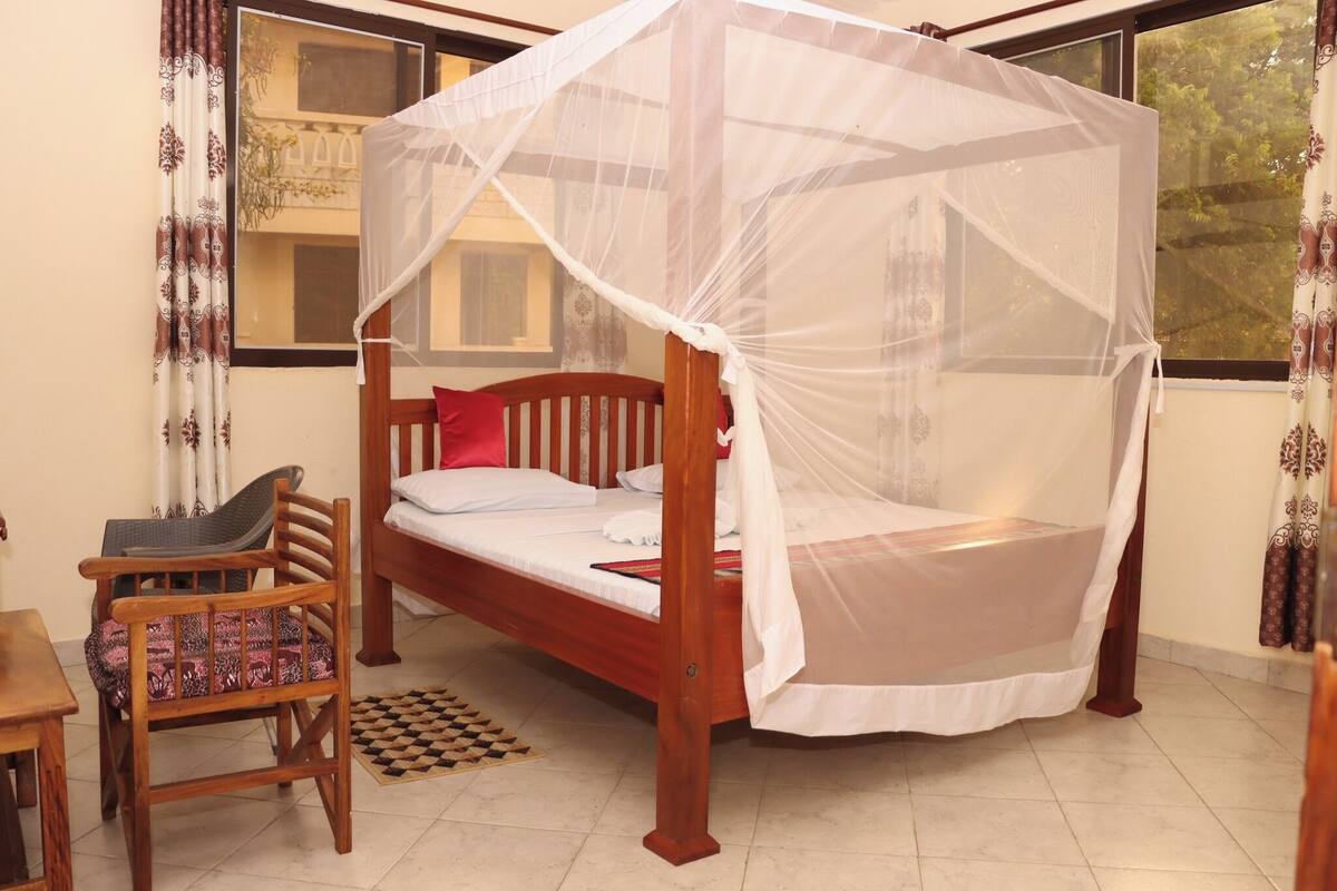 Una habitación con una cama bajo una mosquitera, una silla de madera y una ventana con cortinas.