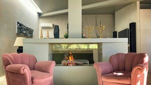 Un salon moderne avec deux fauteuils roses, une cheminée et un téléviseur à écran plat.