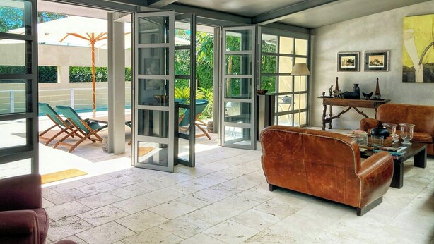 Un vaste espace de vie avec une grande porte vitrée donnant sur une terrasse extérieure, un canapé en cuir et une table basse.