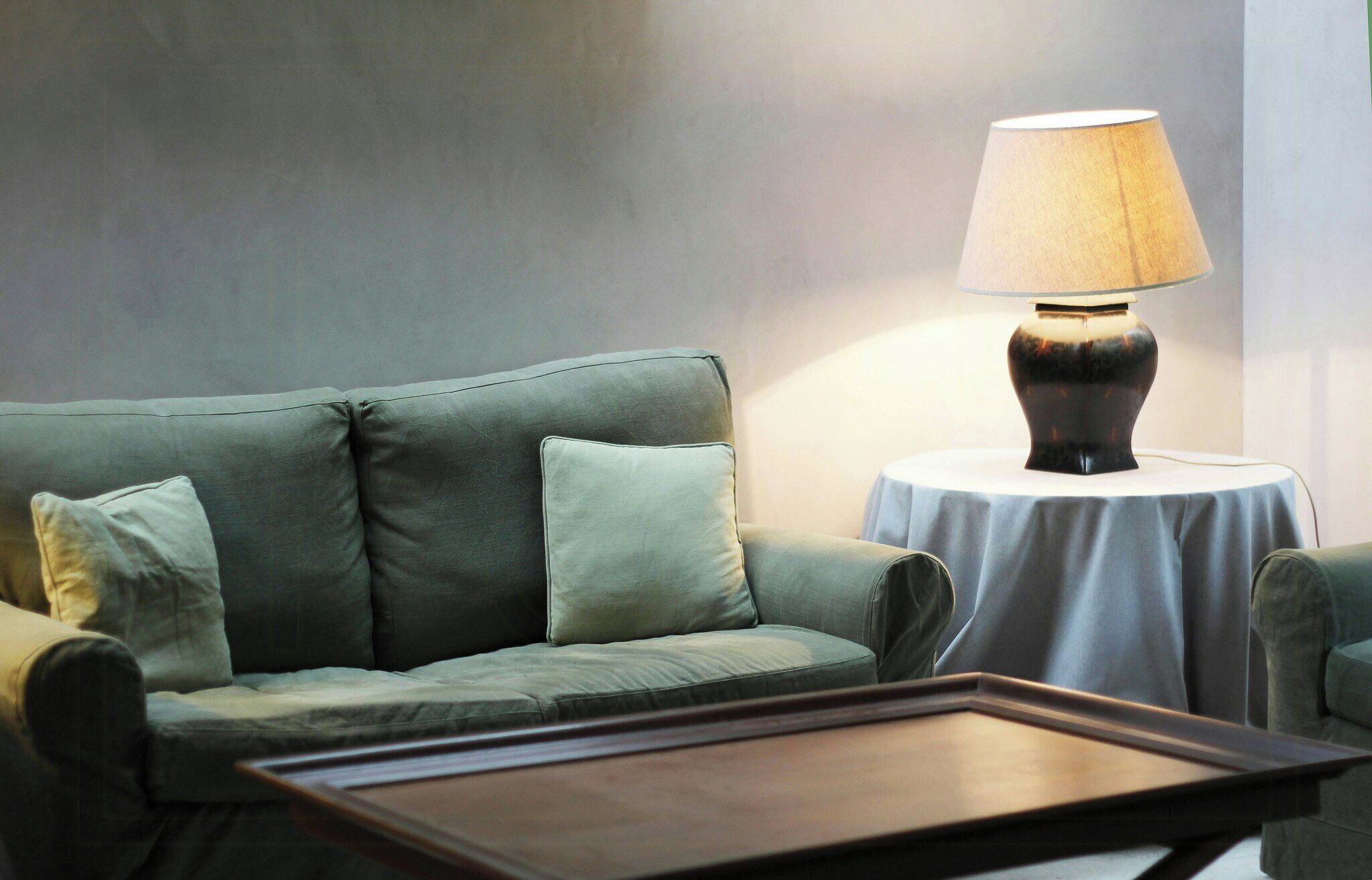 Een groene bank met kussens, een tafel met een lamp en een klein rond tafeltje.