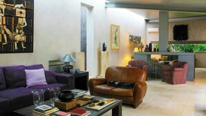 Un salon avec un canapé, des fauteuils, une table basse avec des livres, une lampe et un tableau au mur.