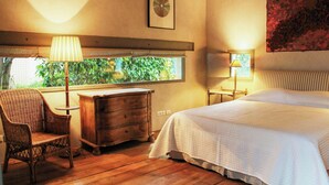 Une chambre à coucher comprenant un lit, une chaise, une commode, une fenêtre donnant sur un paysage verdoyant et un tableau accroché au mur.