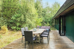 An outdoor wooden deck with a round table and chairs, surrounded by dense greenery. - Summer house in Houstrup with scenic views (Nørre Nebel)