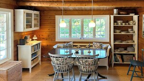 A wooden cabin interior with a dining table, two chairs, a bookshelf, and a window with a view of greenery. - Log cabin on beautiful natural grounds in Hornbæk (Hornbæk)