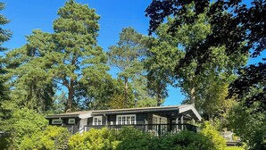 A cabin with a porch, surrounded by dense trees and a well-maintained lawn. - Log cabin on beautiful natural grounds in Hornbæk (Hornbæk)
