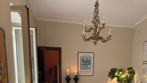 A living room with a chandelier, a sofa, a coffee table, and a dining area with a lamp and decorative items.