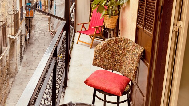 A balcony with a metal table, a red cushion, a wicker chair, and a potted plant.