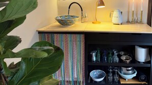 A kitchen with a sink, a bowl, a coffee maker, and a shelf with dishes and a framed picture.