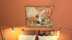 A double bed with white linens, two bedside tables with lamps, and a painting above the bed.