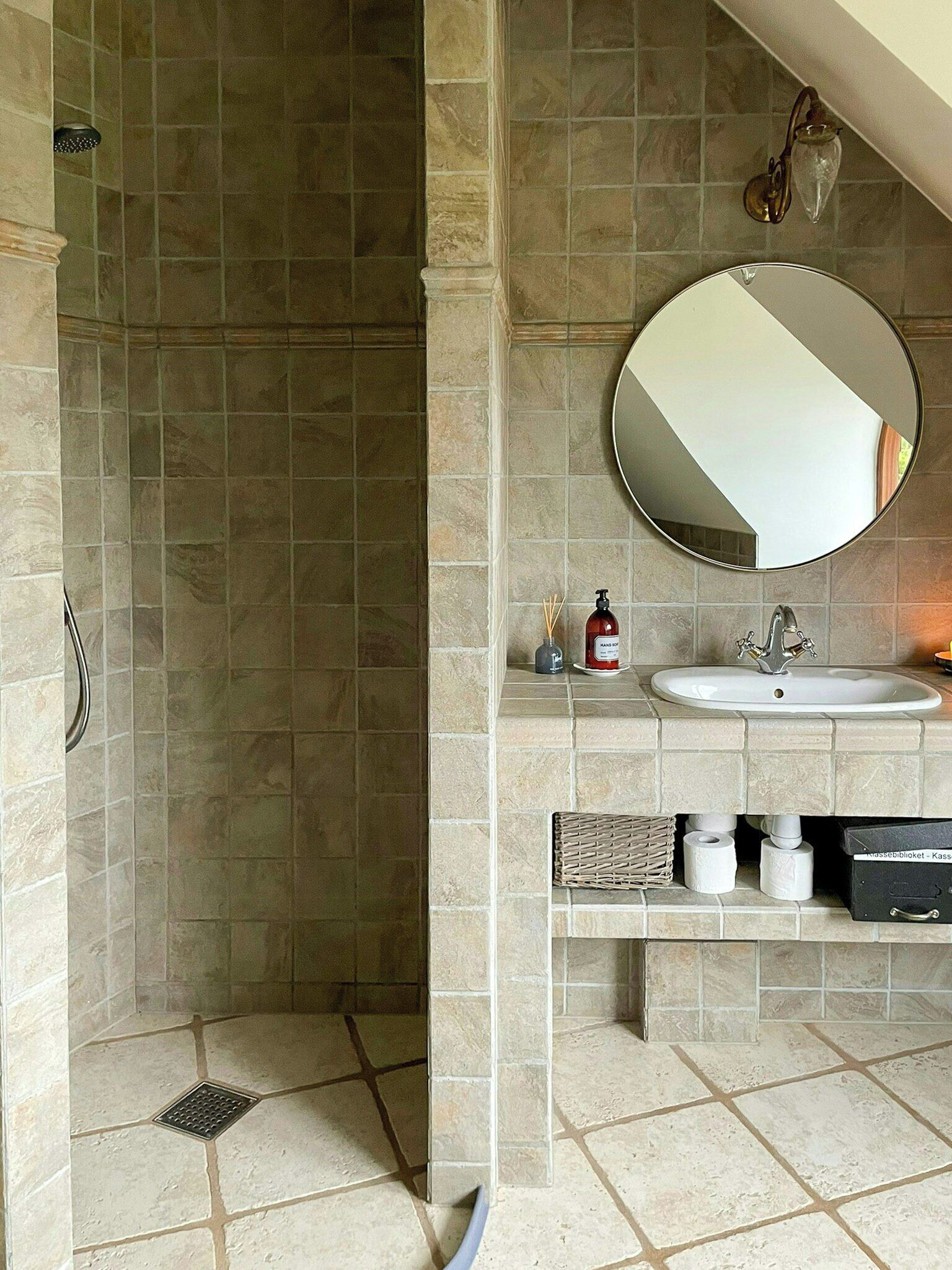 A bathroom with a shower, a sink, a mirror, and toiletries on the counter.