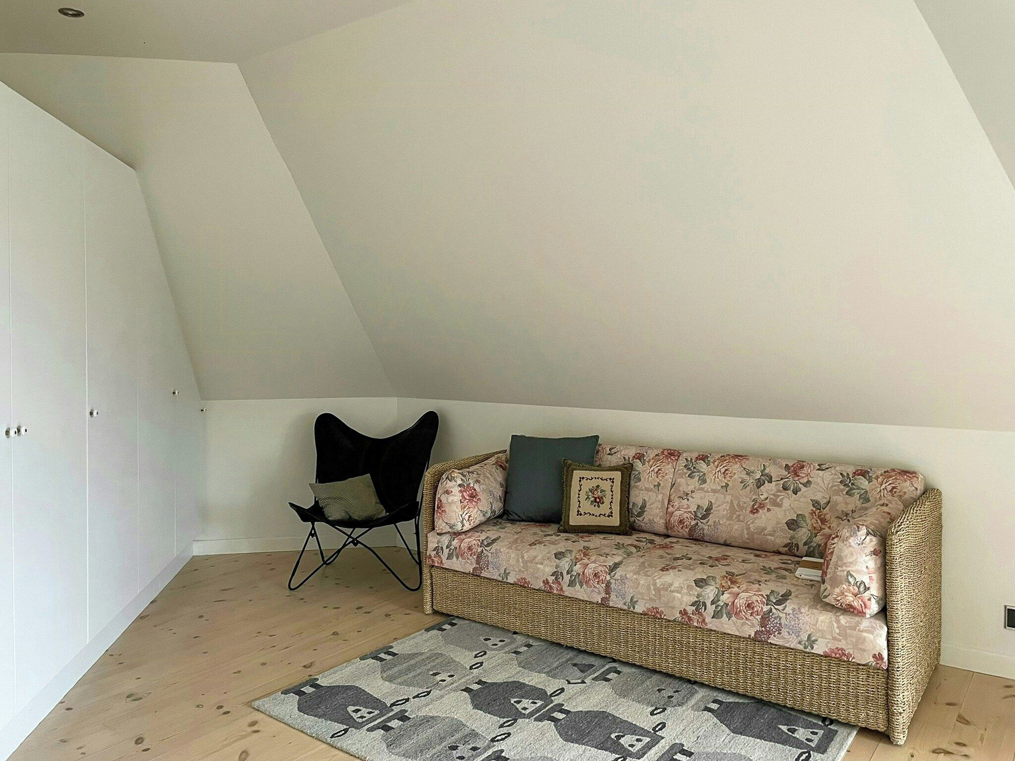 Ein Schlafzimmer im Loft-Stil mit hohen Decken, einem gewebten Sofa, einem schwarzen Sessel und einem gemusterten Teppich.