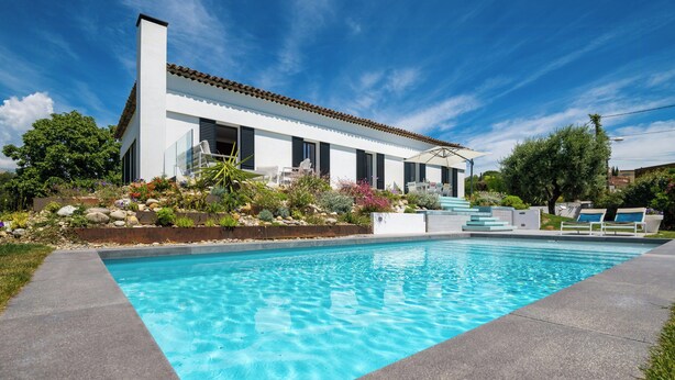 Ett modernt hus med en swimmingpool, utomhusmöbler och en välskött trädgård.