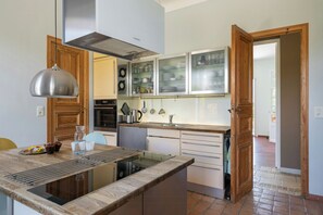 Eine Küche mit einer zentralen Kochinsel, Holzschränken, einer Edelstahl-Dunstabzugshaube und einem Vorratsschrank mit Glastüren.