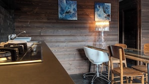 A modern bar area with a wooden wall, two abstract paintings, a bar counter, a white chair, and a table with chairs. - Restored 19th century house with Dolomites view (Sauris di Sopra)