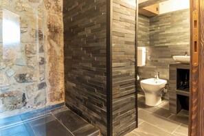 A bathroom with a stone wall, a black tiled wall, a white sink, and a bidet. - Restored 19th century house with Dolomites view (Sauris di Sopra)