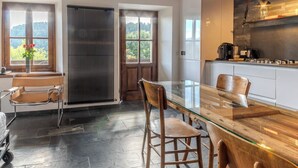 A modern kitchen with a glass dining table, wooden chairs, and a view of the outdoors. - Restored 19th century house with Dolomites view (Sauris di Sopra)