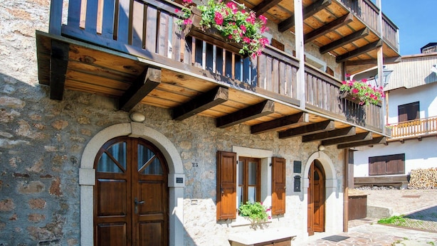 A stone building with wooden balconies, arched doors, and a stone-paved courtyard. - Restored 19th century house with Dolomites view (Sauris di Sopra)