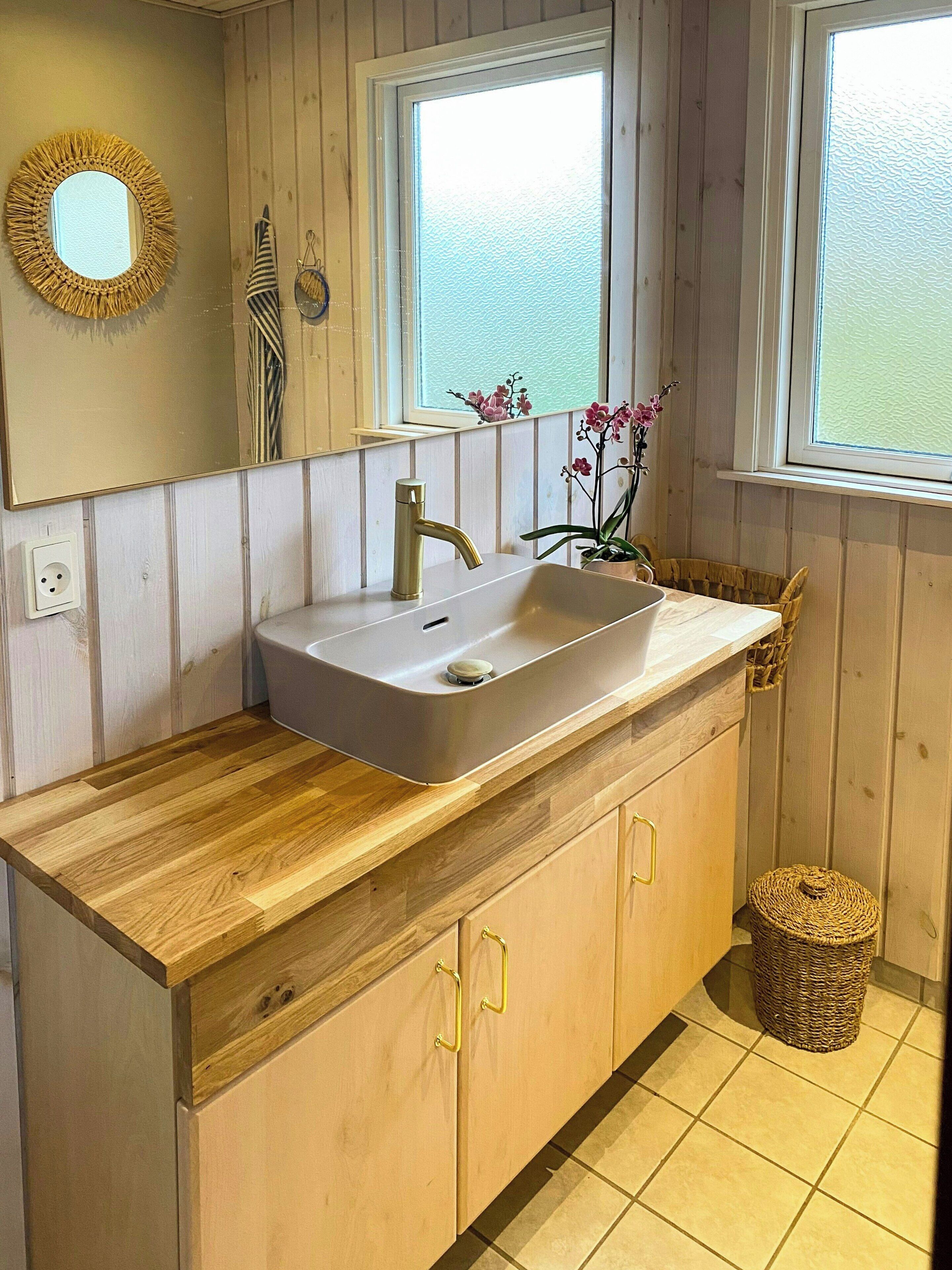 Un baño tipo cabaña de madera con lavamanos, espejo y ventana.